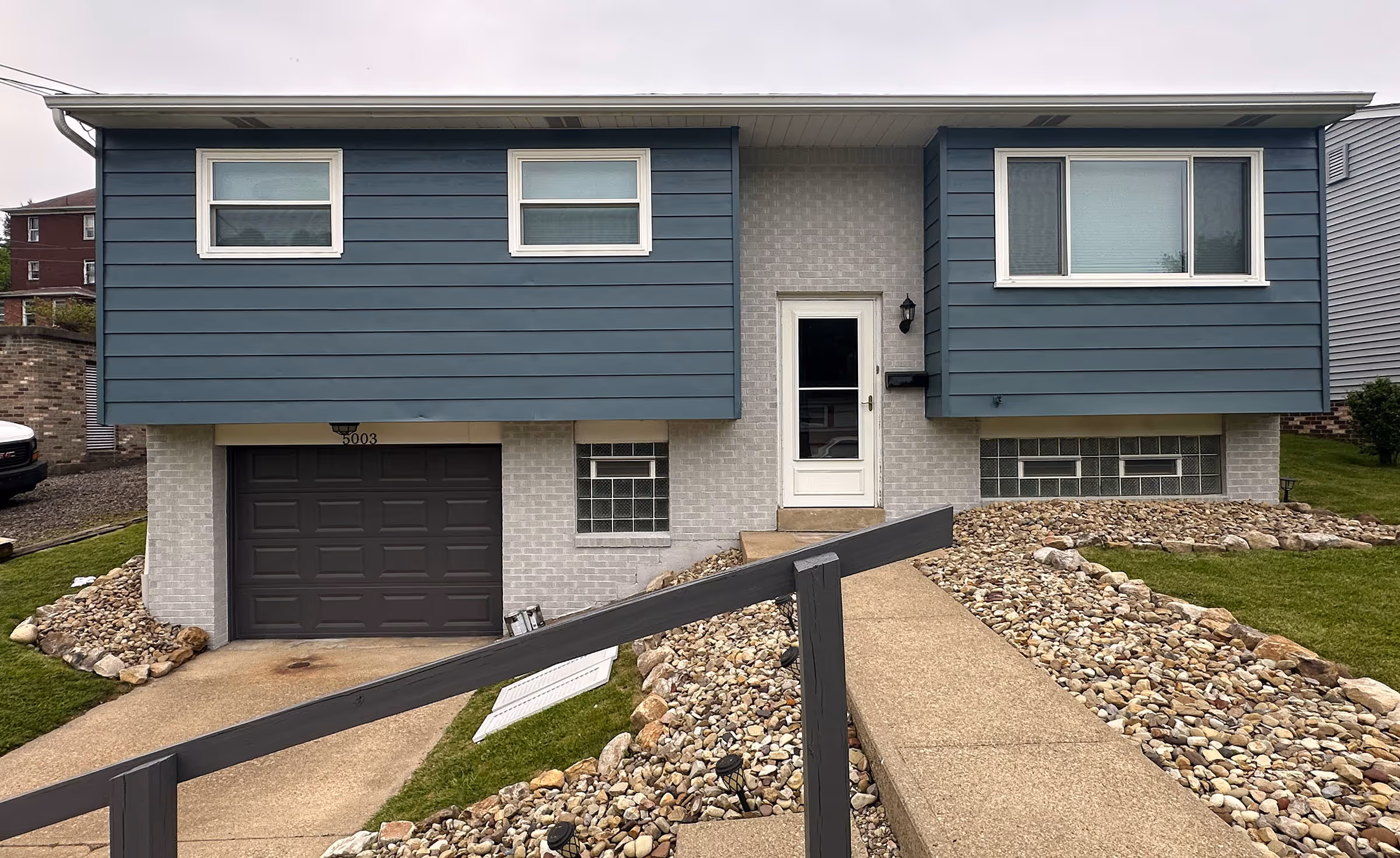 Blue and gray split-level house with white trim, a garage door, and a stone-lined walkway.